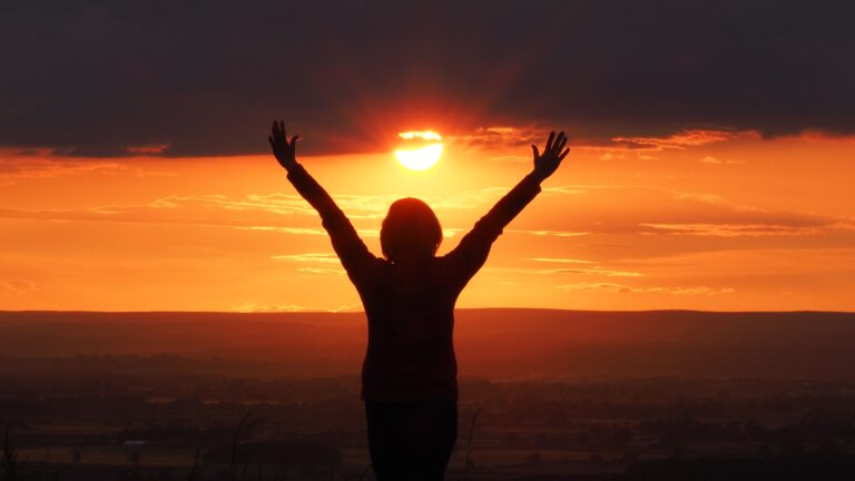 Silhouette of a woman with arms raised against a vibrant sunset in Knapton, England.